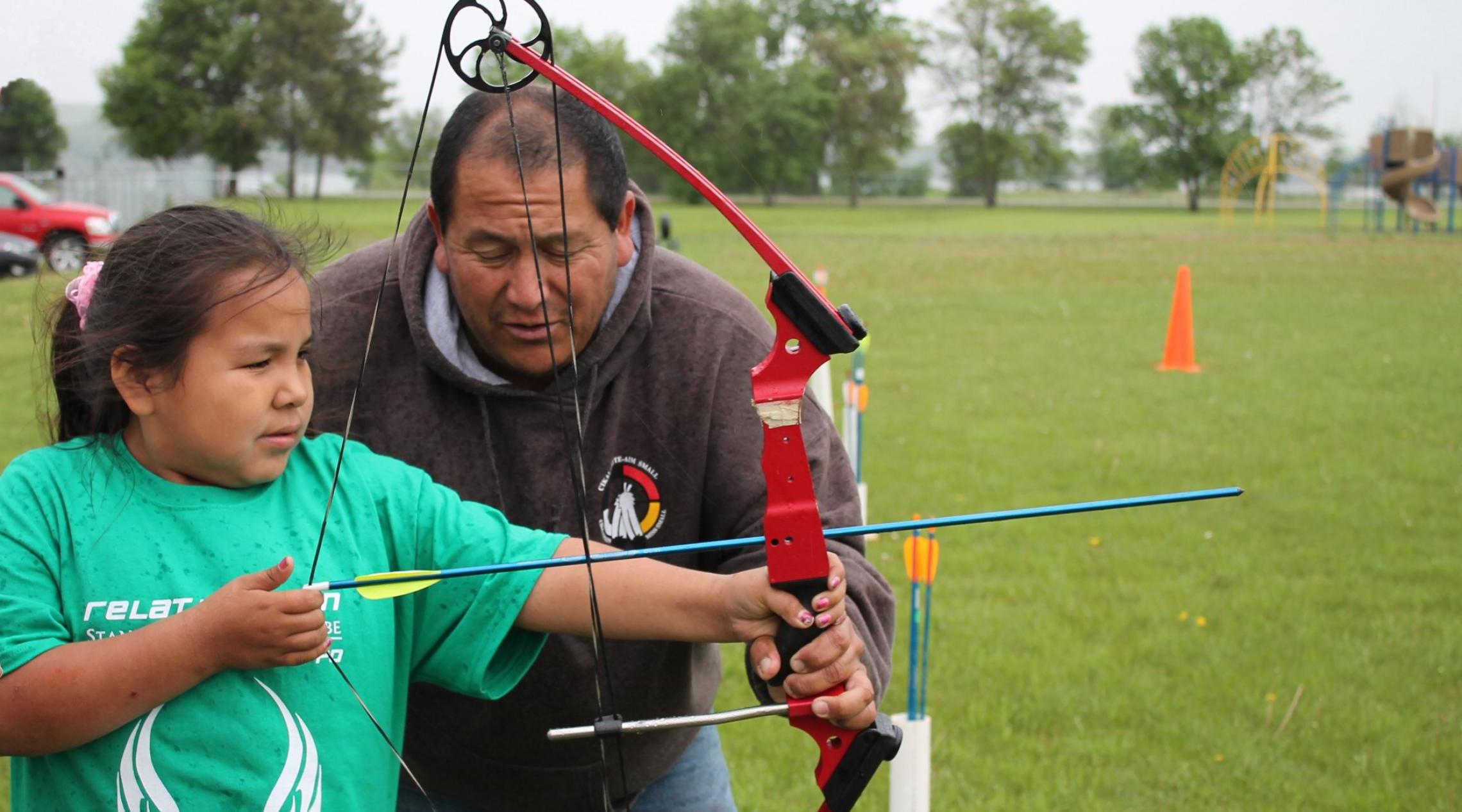 A 4-H volunteer helps a 4-H kid practice archery